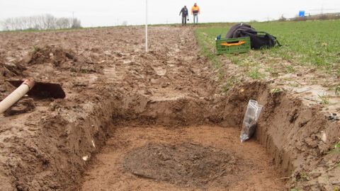 Das Bild zeigt ein vorgeschichtliches Brandgrab dicht unter der Ackeroberfläche.