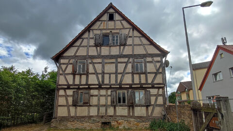 Giebelseite eines Fachwerkhauses mit zwei Vollgeschossen und offen liegendem Fachwerk. Im Erdgeschoss drei Fenster mit Fensterläden, im Obergeschoss zwei Fenster. Ebenfalls zwei mittig liegende Fenster im Giebel.