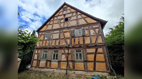 Giebelseite Giebelseite eines Fachwerkhauses mit zwei Vollgeschossen und offen liegendem Fachwerk. Im Erdgeschoss drei Fenster mit Fensterläden, im Obergeschoss zwei Fenster. Bei zwei kleinen Fensteröffnungen im Giebel scheinen die Fensterscheiben zu fehlen. Der Putz ist an einigen Stellen beschädigt.