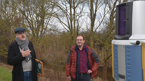 Dr. des. Thomas Becker erläutert die Bedeutung der Zusammenarbeit zwischen der hessenARCHÄOLOGIE und den beteiligten Universitäten. Foto. Dr. des. Thomas Becker und Prof. Dr. Markus Scholz mit Vermessungsgerät.