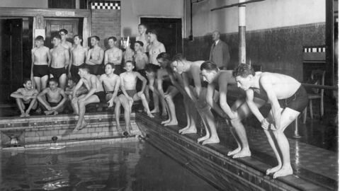 Viele Badegäste sitzen am Beckenrand des Schwimmbads. Historische Aufnahme von 1934.