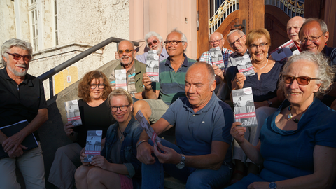 Hinter dem Namen "Kulturtaucher" steckt ein breites Spektrum an unterschiedlichen Programmen und Veranstaltungen, die jede Menge Unterhaltung bieten Ulrich Lang und weitere Menschen auf einer Treppen halten einen Flyer mit der Aufschrift Kulturtaucher in die Kamera
