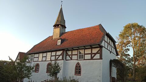 Die Alte Kirche in Bürgeln Weiß verputztes Gebäude mit Fachwerk im Obergeschoss und rotem Ziegeldach