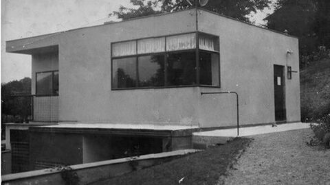 Schwarz-Weiß-Bild von einem Gebäude mit flachem Dach und großen Fenstern.