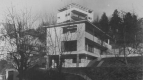 Schwarz-Weiß-Bild eines dreistöckigen Gebäudes mit großen Fenstern und langen Balkonen. Ein Dach ist nicht sichtbar.