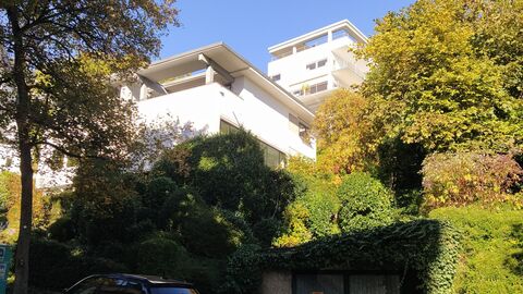 Foto eines weiß gestrichenen Gebäude mit großen Fenstern und Loggia. Das Gebäude ist von vielen Bäumen und Büschen umgeben.