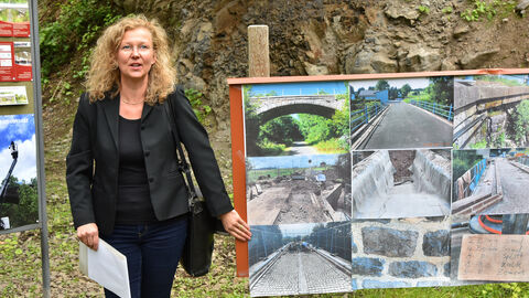 Man sieht Dagmar Zinn, die die Maßnahme als Architektin begleitet hat, vor dem Hintergrund der Brücke. Sie erklärt das Bauvorhaben mit Hilfe einer Fotodokumentation.  