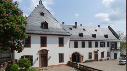 Der Eltzer Hof in Eltville gehört zu den vorgestellten Beispielprojekten. Weiß verputztes Gebäude mit rötlichen Tür- und Fensterrahmungen sowie einem zweigeschossigen Dach mit Schieferdeckung.
