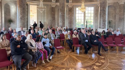 Mehrere Stuhlreihen, in denen die Zuhörenden sitzen.