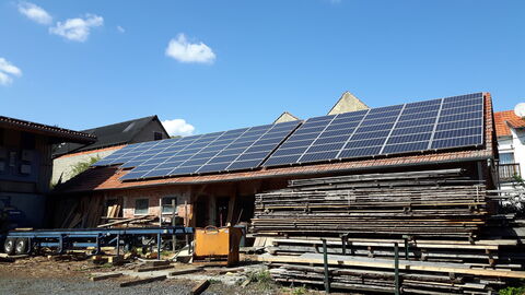 Kuh- und Schweinestall Flaches eingeschossiges Gebäude mit Satteldach und großflächiger Solaranlage. Davor ein großer Stapel Holz.