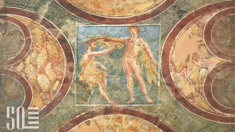 Dieses Bild zeigt eine römische Wandmalerei im Römerkastell Saalburg, die aus dem Limeskastell Echzell in der Wetterau stammt. Vier Schilde rahmen die Darstellung des sitzenden Dädalus auf blauem Grund, der seinem Sohn Ikarus mit Wachs Flügel aus großen Federn an die Arme klebt.