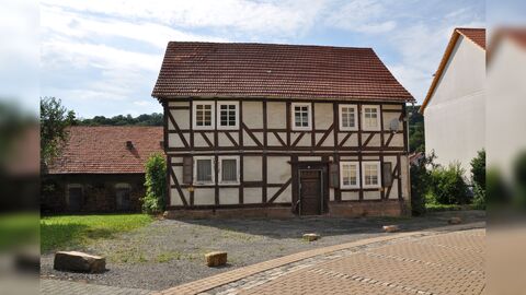 Blick vom Ortskern auf das Wohnhaus Blick auf die Traufseite eines zweigeschossigen Fachwerkwohnhauses mit Sichtfachwerk. Im Hintergrund Wirtschaftsgebäude.