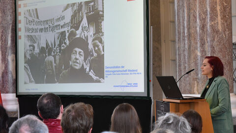 Man sieht Katharina Marschall am Rednerpult in der Rotunde des Biebricher Schlosses, dem früheren Festsaal der Sommerresidenz der Fürsten und späteren Herzöge von Nassau am Rheinufer in Biebrich. 