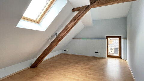 Heller Raum mit Dachschräge, sichtbaren Dachbalken und Parkettboden