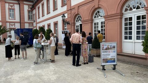 Bei einem kleinen Umtrunk tauschten sich die Gäste untereinander aus, um die Impressionen und Erkenntnisse der Ausstellung rege zu diskutieren Die Gäste stehen draußen vor dem Schloss und tauschen sich aus