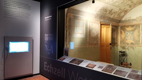 Der Blick auf die neue Präsentation der Wandmalerei. Auf der Rückwand der Malerei sind vier Szenen von Schildern gerahmt. Rechts ist der sitzende Dädalos dargestellt, der seinem Sohn Ikaros Flügel mit Wachs an Arme und Beine klebt.  Die Szene links spielt ebenfalls auf Kreta: Theseus ist in das Labyrinth des Stiermenschen Minotauros eingedrungen und tötet das Ungeheuer. In der Mitte begegnet Fortuna mit Füllhorn und Rad dem Herkules im Löwenfell, der lässig auf einem Baumstamm lehnt und in der Armbeuge sein