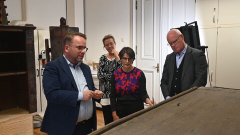 v.l.: Staatsminister Timon Gremmels betrachtet mit den Restauratorinnen Christine Kenner und Christiane Weber sowie Prof. Dr. Markus Harzenetter, Präsident des Landesamtes für Denkmalpflege Hessen, betrachten einen seltenen mittelalterlichen Schrank.