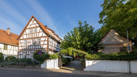 Haupthaus und Eingangstor Giebelständiges Fachwerkaus, anschließend eine weiße Mauer mit begrüntem Torbogen