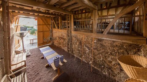 Die Scheune Hoher Raum mit Tisch und Bänken. Im hinteren Bereich schließt eine Empore oberhalb einer Bruchsteinmauer an
