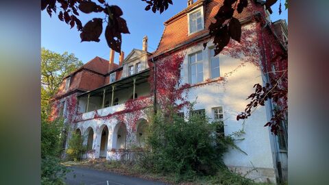 Hauptfassade. Weiß verputzte Fassade eines großen Gebäudes mit zwei Vollgeschossen und einem rot eingedeckten Mandarddach. die Fassade ist symmetrisch aufgebaut 