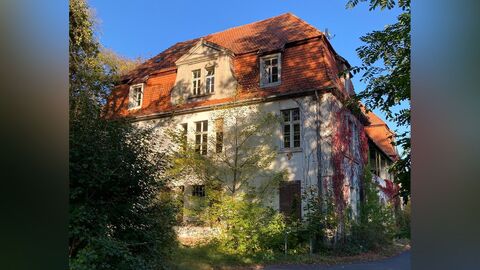 Seitenfassade. Weiß verputzte Fassade eines großen Gebäudes mit zwei Vollgeschossen und einem rot eingedeckten Mandarddach. die Fassade ist symmetrisch aufgebaut 