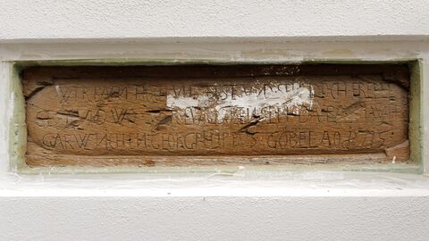 Der freigelegte Balken mit der Bauinschrift Holzbalken mit Inschrift, drumherum ist die Wand verputzt