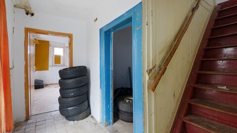Innenraum mit historischer Treppe Schmale, rote Holztreppe rechts im Bild, sowie ein Flur mit mehreren Türen, die in verschiedenen Farben bunt gestrichen sind.