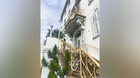 Treppe mit gold verziertem Geländer führt zu einer Eingangstür mit bunter Verzierung