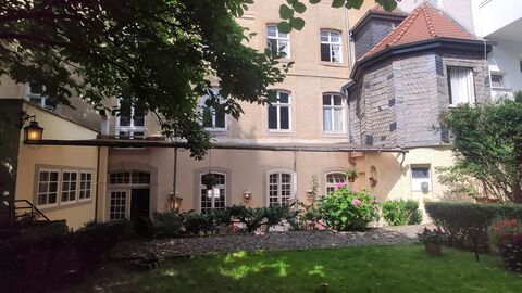 Baumzweige im oberen liunken Bildteil. Blick auf eine Hauswand mit braunem Putz und einen kleinen verschieferten Anbau