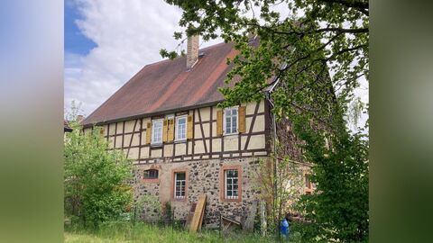 Großvolumiges Fachwerkhaus mit Erdgeschoss aus Bruchstein und einem Satteldach mit roter Biberschwanzeindeckung.