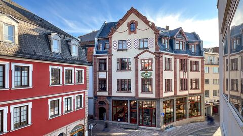 Das Wohn- und Geschäftshaus steht in einer markanten Blickachse in der Fuldaer Innenstadt Großvolumiges Haus mit drei Vollgeschossen und einem Mansarddach. Das hohe Erdgeschoss ist durch Steinputzflächen besonders hervorgehoben