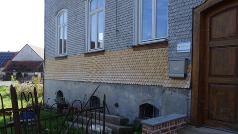 Straßenseite mit Haupteingang Verschindelte Fassade mit Segmentbogenfenstern und einer Holztür.